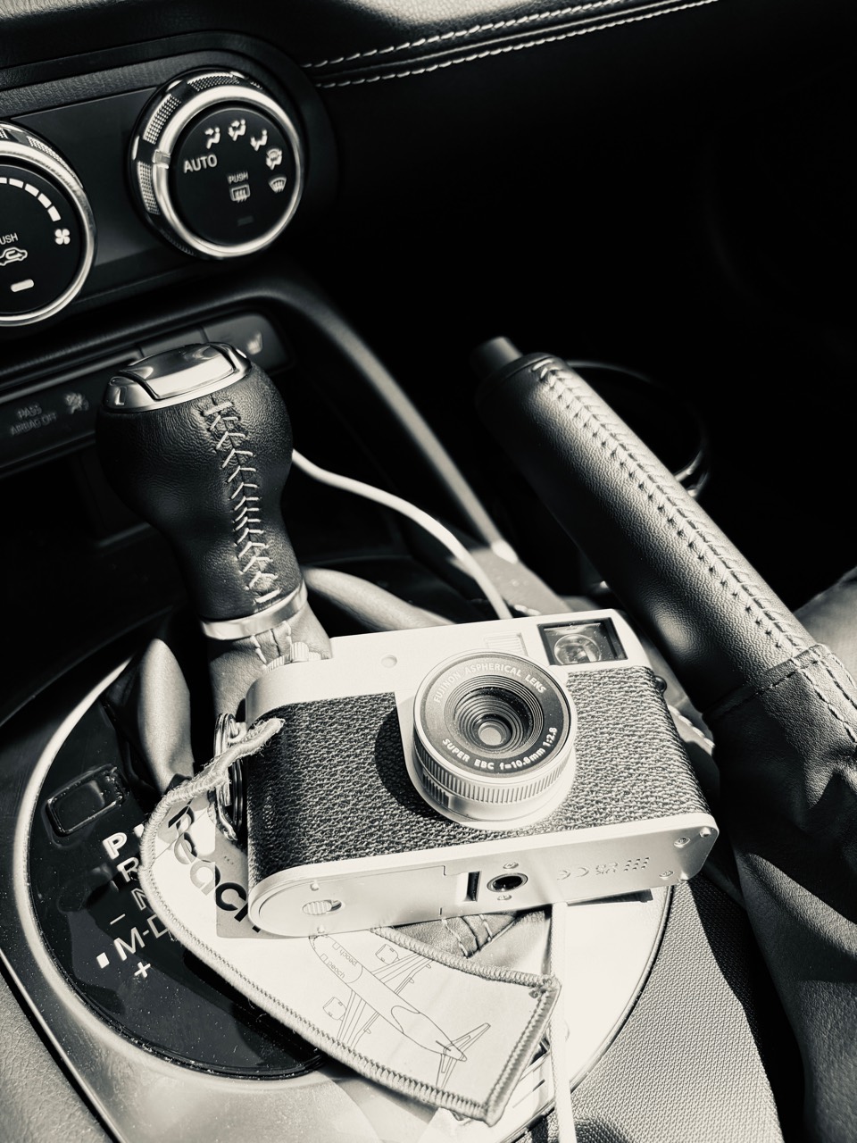 Black-and-white photo of a Fujifilm camera beside the gearshift and handbrake inside a car
